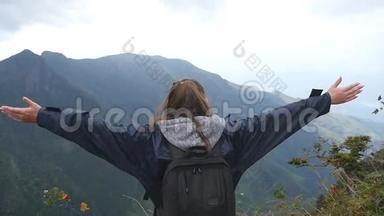 年轻的女徒步旅行者，背包伸向<strong>山顶</strong>，举起双手。 穿着雨衣的女游客<strong>站在</strong>